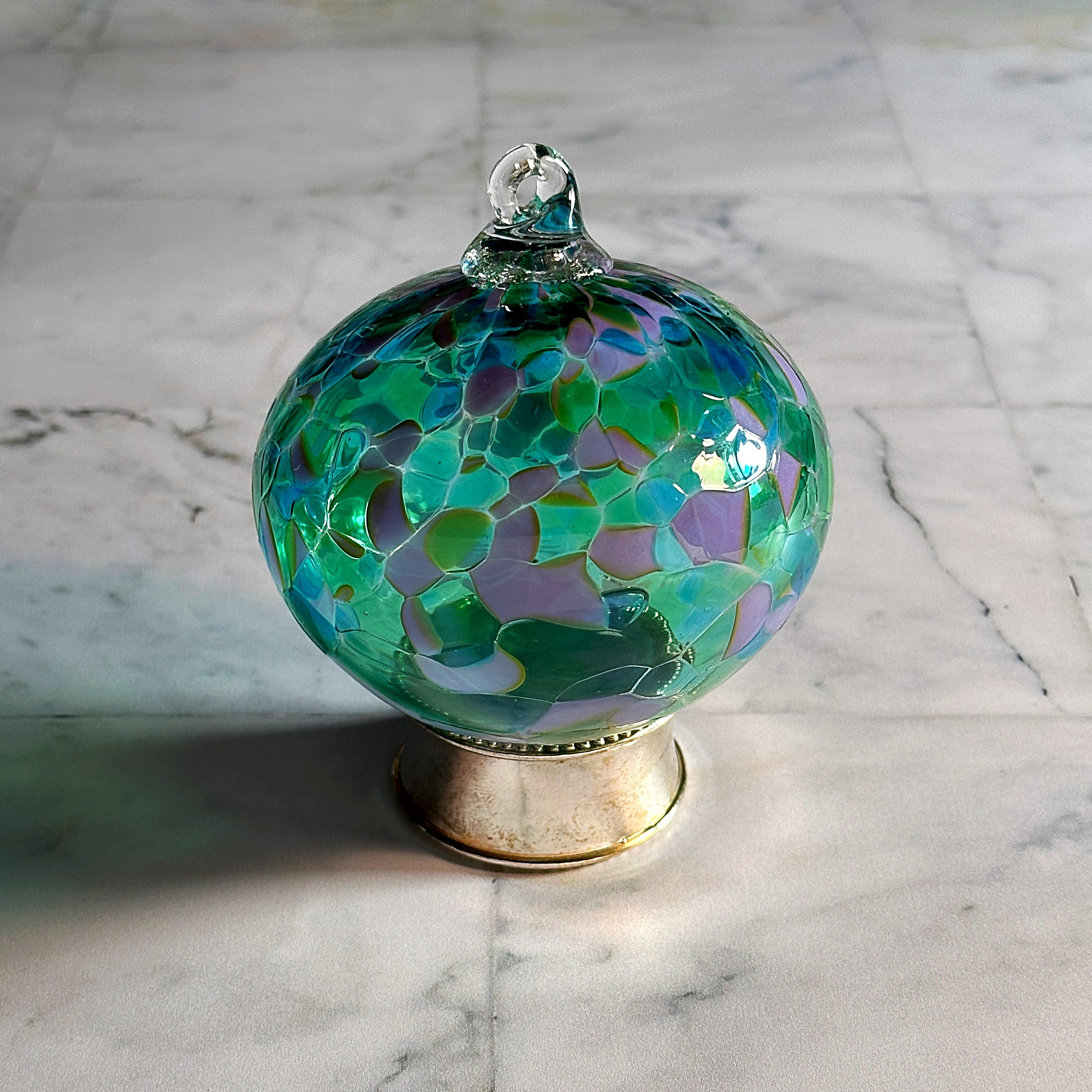 green and lavender round hand-blown glass ornament on display